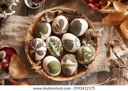 Raw Easter eggs with herbs attached to them in a basket, ready to be dyed with onion peels, top view