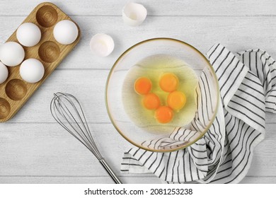 Raw eggs and whisk on a wooden background, top view. Pie or cake recipe, breakfast concept, top view.