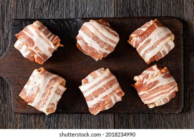 raw english meatballs, uncooked faggots are made of minced offal and meat wrapped in streaky bacon on a rustic cutting board, flat lay, close-up