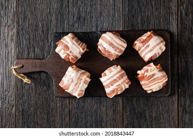 raw english meatballs, uncooked faggots are made of minced offal and meat wrapped in streaky bacon on a rustic cutting board, flat lay