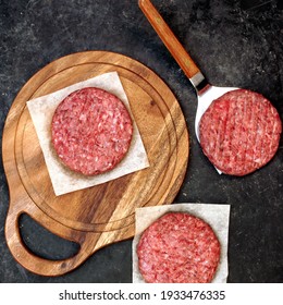 Raw Farmers Beef Pork Burgers And Grill Tools On Wooden Board, Top View. Raw Ground Beef Meat Steak Burger Cutlets On Black Table Background, Overhead View. Homemade Uncooked Beef Pork Burgers.