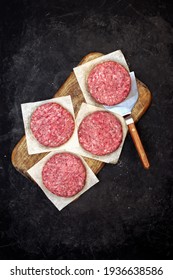 Raw Farmers Beef Pork Burgers And Grill Tools On Wooden Board, Top View. Raw Ground Beef Meat Steak Burger Cutlets On Black Table Background, Overhead View. Homemade Uncooked Beef Pork Burgers.