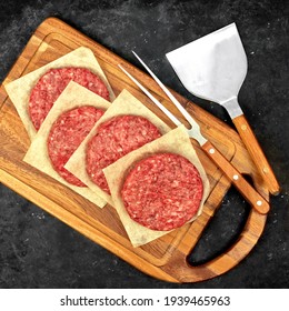 Raw Farmers Beef Pork Burgers And Grill Tools On Wooden Board, Top View. Raw Ground Beef Meat Steak Burger Cutlets On Black Table Background, Overhead View. Homemade Uncooked Beef Pork Burgers.