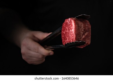 Raw filet Mignon steak in tongs in hand, cooking meat on the grill
