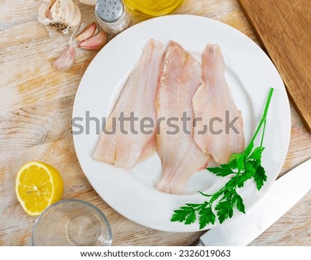 Raw fish with condiments, red perch fillet on plate with garlic and parsley on wooden surface