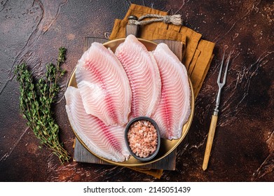 Raw fish fillet of tilapia in a plate with spices. Dark background. Top view.