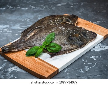 Raw fish flounder with salt and basil on a kitchen board close-up