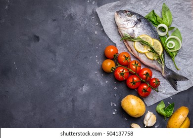 Raw Fish With Fresh Ingredients Ready To Cook. Fish, Lemon, Herbs, Potato, Tomatoes. Ingredients For Cooking On Dark Rustic Background. Space For Text. Diet And Healthy Food. Fish Background. Top View