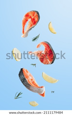 Raw fish salmon steak with lemon and rosemary on blue background. Food levitation concept