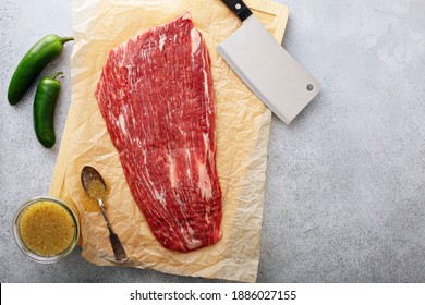 Raw flank steak on a cutting board with a meat cleaver ready to be marinated