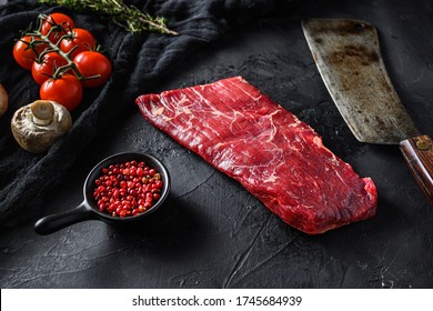 Raw, flap or flank, also known Bavette steak near butcher knife with pink pepper and rosemary. Black stone background. Side view vertical