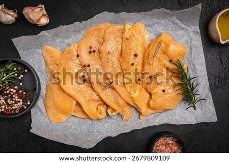 Raw free range and corn fed chicken carved in slices. Corn fed yellow chicken breast on paper on dark background, top view
