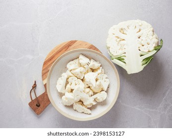 raw fresh cauliflower cut in half on the countertop next to a bowl on a wooden cutting board with chunks cut in florets
