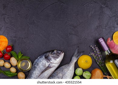 Raw Fresh Dorado Fish With Brussels Sprouts, Tomatoes, Lemon, Young Potato, Greens, Bread, White Wine Bottle And Olive Oil On Dark Background. View From Above, Top Studio Shot