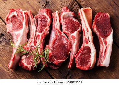 Raw fresh lamb ribs and rosemary on wooden cutting board on dark background