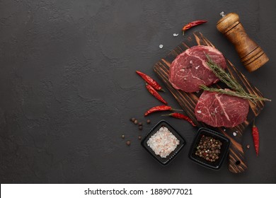 Raw fresh meat. Beef steaks on cutting board and spices on black slate background. Top view with copy space. Steak menu
