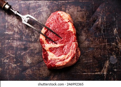 Raw Fresh Meat Ribeye Steak And Meat Fork On Dark Metal Backgrou