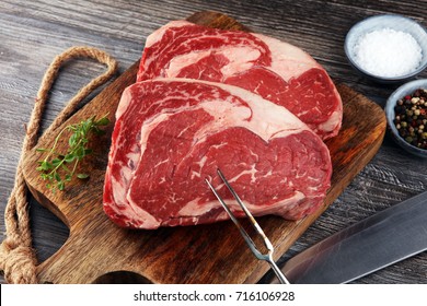Raw fresh meat Ribeye Steak, seasoning and meat fork on dark background - Shutterstock ID 716106928