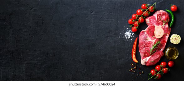 Raw fresh meat steak with cherry tomatoes, hot pepper, garlic, oil and herbs on dark stone, concrete background. Banner