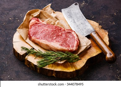 Raw Fresh Meat Striploin Steak And Meat Cleaver On Butcher Block On Dark Background