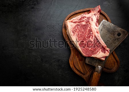 Raw fresh meat T-bone beef Steak and butcher knife on black background, top view