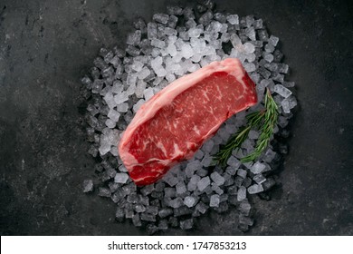 Raw fresh New York beef steak on ice with herbs and rosemary, top view and copy space