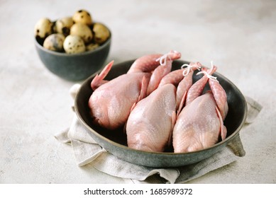 Raw fresh quail birds in a black plate and quail eggs.