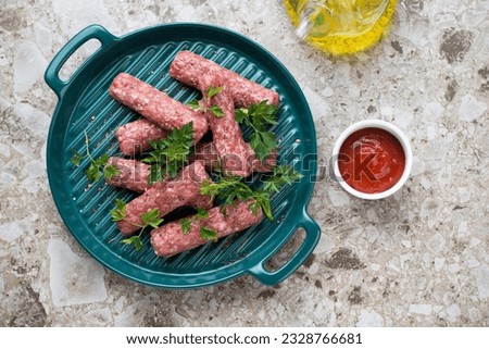 Raw fresh serbian cevapi or cevapcici on a green serving tray, flat lay on a light-brown granite background, horizontal shot