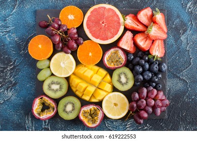 Raw fruits platter: oranges, lemons, kiwis, grapefruits, strawberries, grapes, blueberries, passion fruit, mango on the black slate on the dark blue background, top view - Powered by Shutterstock