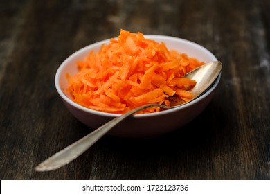 Raw grated carrot on a wood table with a spoon