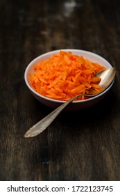 Raw grated carrot on a wood table with a spoon