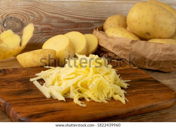 Raw grated potato on wooden cutting board\
background. Grate and sliced potatoes pile for swiss potato or\
pancakes on vintage chopping board\
closeup