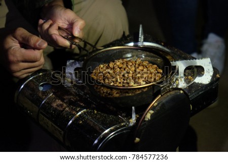 Raw green coffee beans are roasted over compact gas stove by hands with a sieve to the level' light roast'  (after the first crack level) 