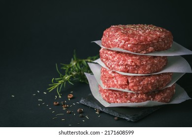 Raw ground beef burger patties separated by baking paper on a black background - Shutterstock ID 2171608599