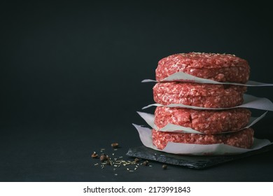 Raw ground beef burger patties separated by parchment paper on a black background - Powered by Shutterstock