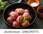 Raw ground beef meatballs in black bowl, food preparation