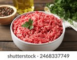 Raw ground meat in bowl, parsley, spices and oil on wooden table, closeup