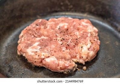 A Raw Ground Pork Sausage Breakfast Patty Beginning To Cook In A Cast Iron Skillet