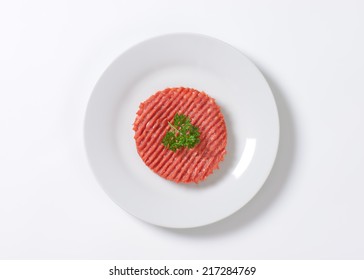 Raw Hamburger Patty With Parsley On White Plate