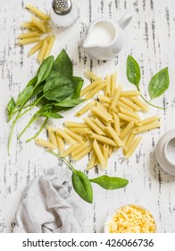 Raw Ingredients For Making Pasta With Spinach Cream Sauce - Penne Pasta, Fresh Spinach, Cream, Cheese And Spices On A Light Wooden Background