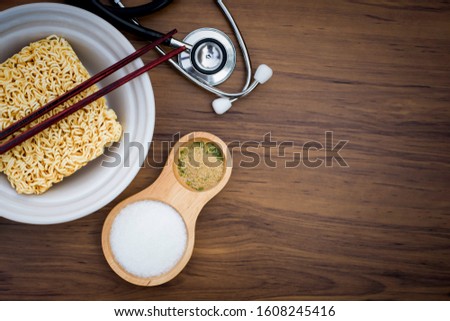 Raw instant noodles or dry noodle with monosodium glutamate (MSG ), ingredients in wooden spoon and medical stethoscope isolated on the wood table background. Unhealthy food concept. Top view.