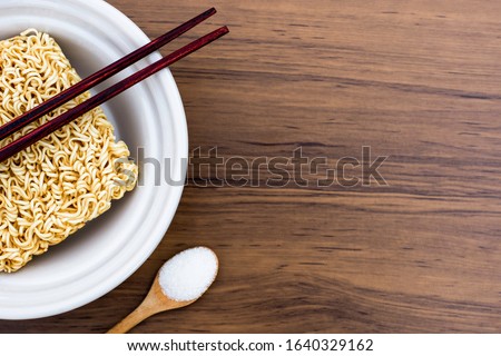 Raw instant noodles or dry noodle with monosodium glutamate (MSG )  in wooden spoon isolated on the wood table background. Top view. Flat lay. 