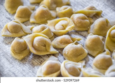 Raw italian cappelletti, fresh homemade pasta stuffed with cheese and meat on rustic wood table. Natural light