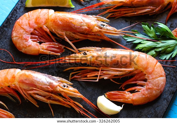 Raw jumbo shrimp with garlic,\
lime and parsley on a black stone slab for the grill\
horizontal
