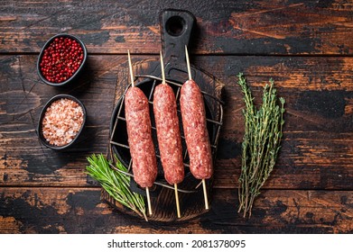 Raw kofta or lula kebabs skewers on a grill with herbs. Dark wooden background. Top view