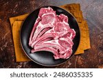 Raw lamb chops, fresh mutton meat cutlets on a ribs. Dark background. Top view.