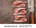 Raw lamb chops with salt, pepper and herbs over black brown background with Meat cleaver and fork near. Top view.