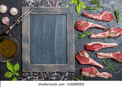 Raw lamb chops with salt, pepper and rosemary over black background. chalk board near. Top view,  copy space.