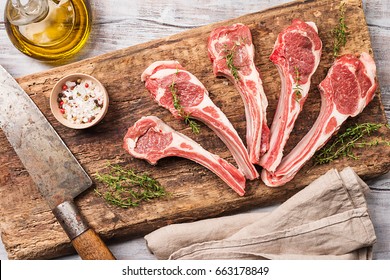 Raw lamb chops with salt, pepper and herbs over white wooden background with vintage chef knife near. Top view.