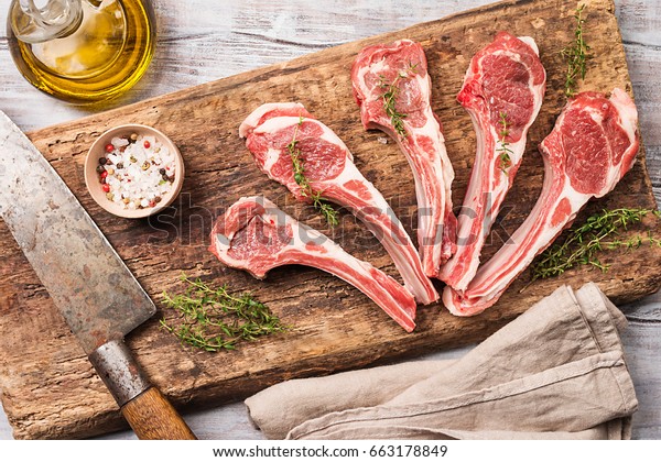 Raw lamb chops\
with salt, pepper and herbs over white wooden background with\
vintage chef knife near. Top\
view.